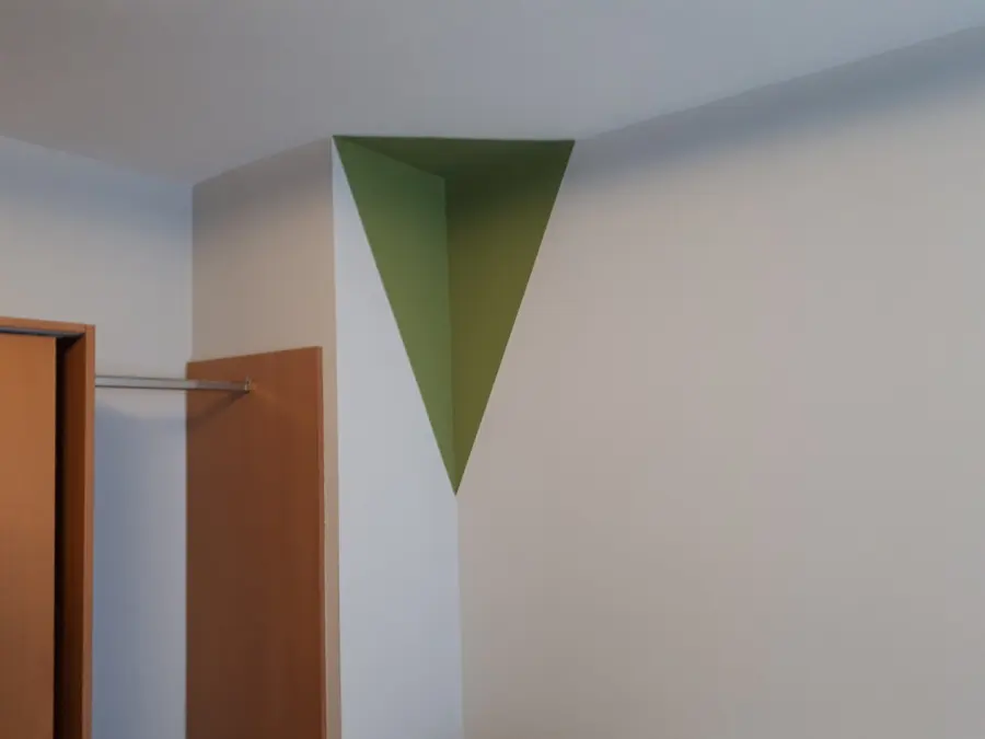 Weiße Zimmerecke mit exakt angelegtem grünem Dreieck, das über Wand und Decke verläuft