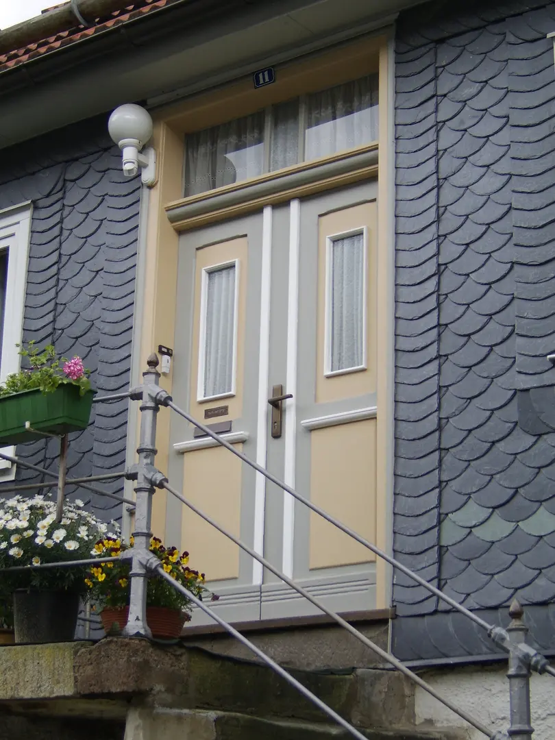 Hauseingang mit beige-weiß lackierter Haustür, Sandsteingewände und dunkelgrauer Schieferfassade