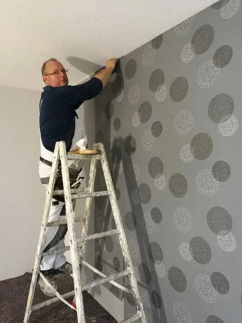 Maler auf einer Leiter beim Tapezieren einer grauen Mustertapete mit Kreisdekor