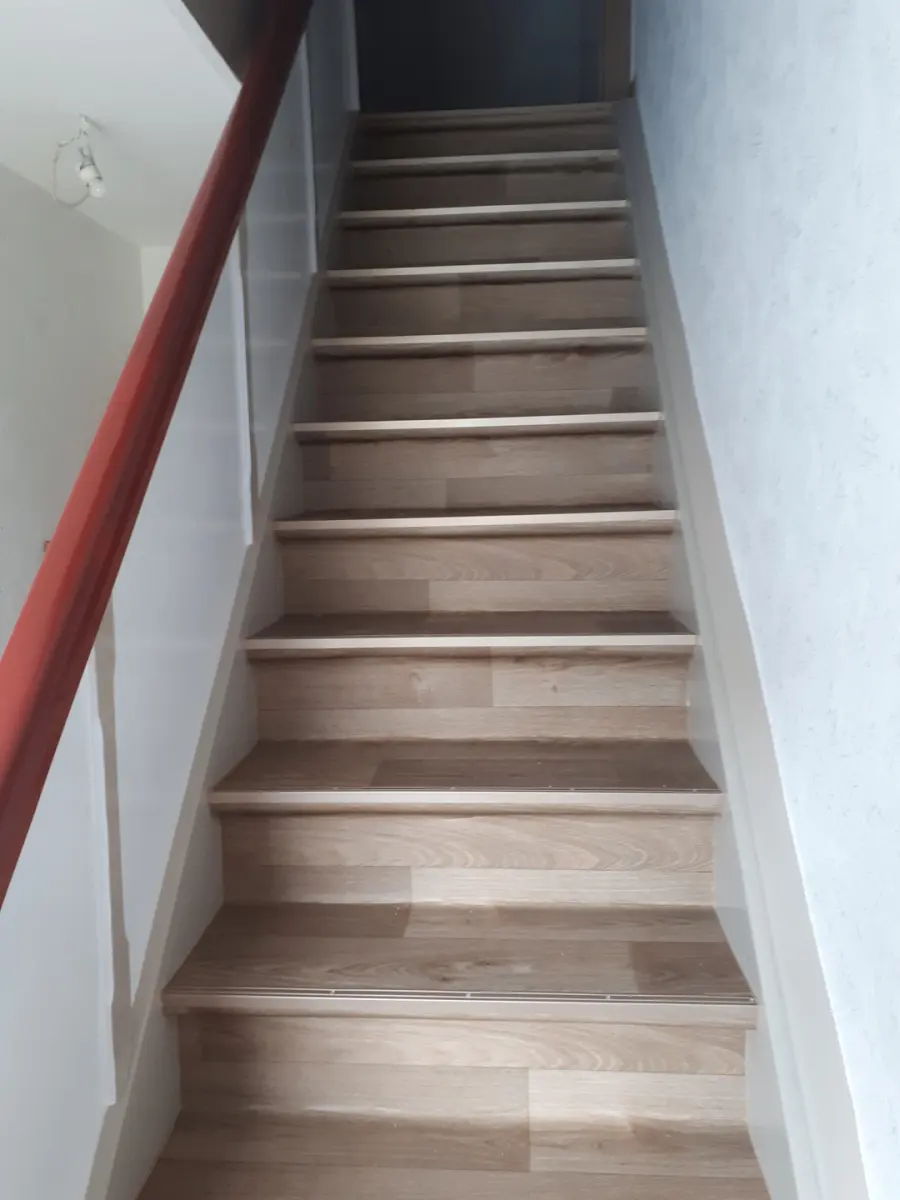 Frisch renovierte Treppe mit hellen Holzstufen, weißen Setzstufen und rot lackiertem Handlauf